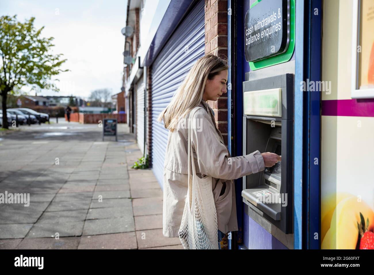 Eine Seitenansicht einer kaukasischen Frau mit mittlerem Erwachsenen, die an einem Geldautomaten auf einer Straße in der Stadt eine Debitkarte verwendet, in legerer Kleidung. Stockfoto