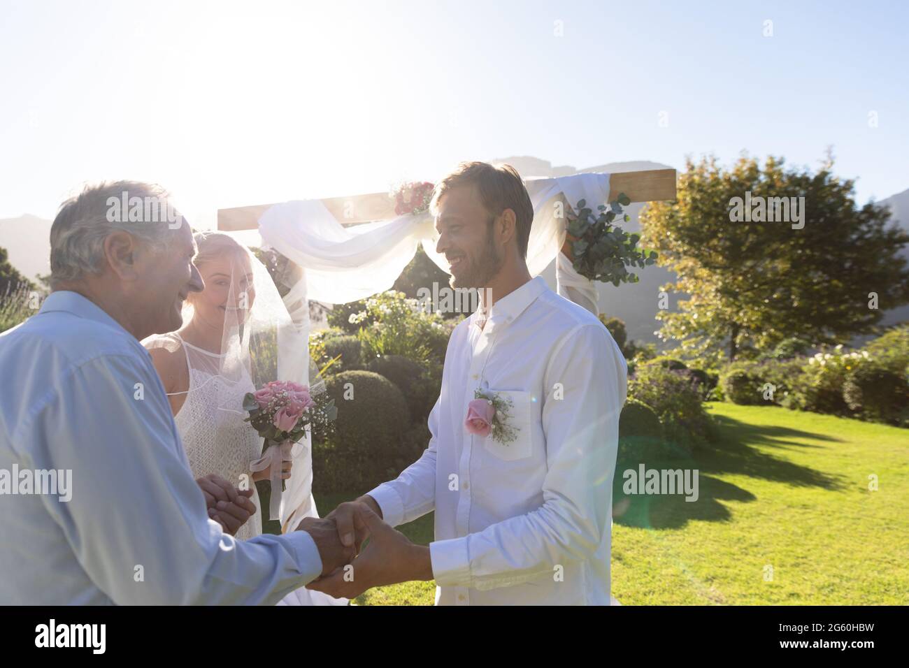 Glückliche kaukasische Braut und Bräutigam, die heiraten, schüttelt sich die Hände mit dem Hochzeitsoffizier Stockfoto