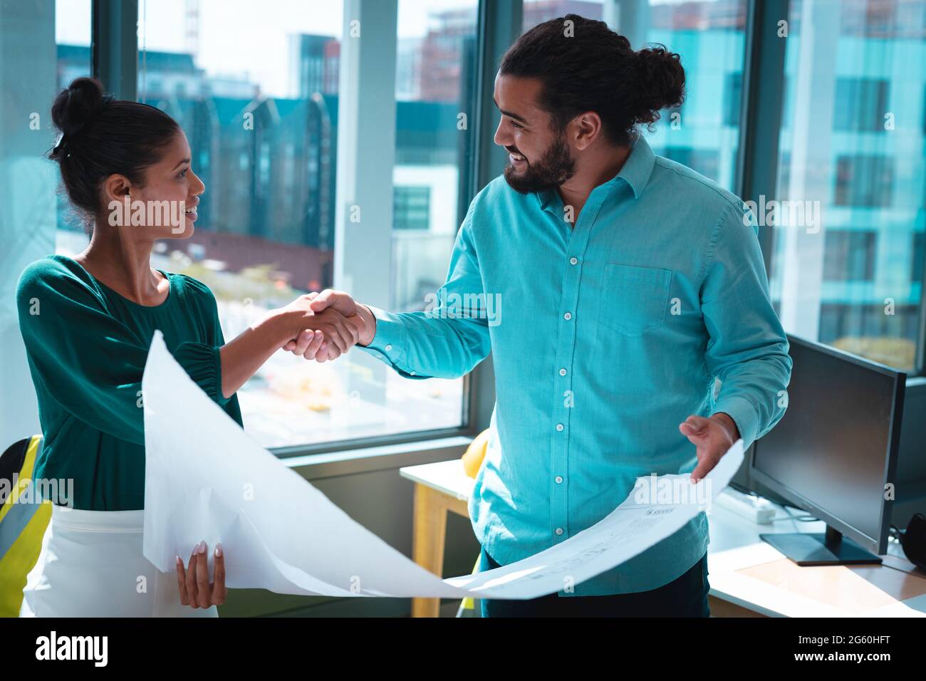 Zwei verschiedene Geschäftsleute schütteln sich die Hände, diskutieren gemeinsam und halten ein Schema ab Stockfoto