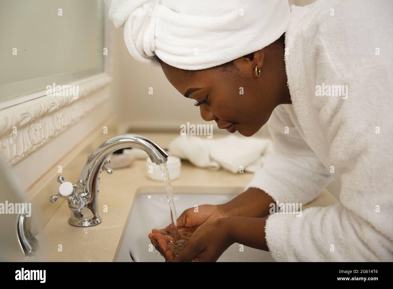 afroamerikanische Frau im Badezimmer mit Handtuch auf dem Kopf, stehend an der Waschtisch-Waschküche Stockfoto