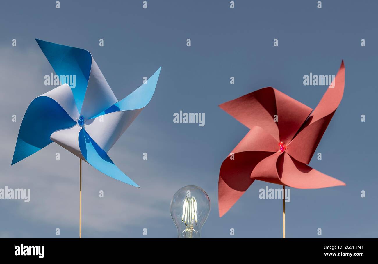 Zwei bunte Papierräder und eine beleuchtete Glühbirne, machen das Konzept der sauberen Windenergie, gegen den blauen Himmel Stockfoto