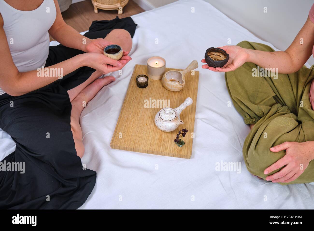 Zwei Frauen halten eine chinesische Teezeremonie auf einem Heimbett im Schlafzimmer, einem Tablett mit einer Teekannen, Tassen und Kerzen ab Stockfoto