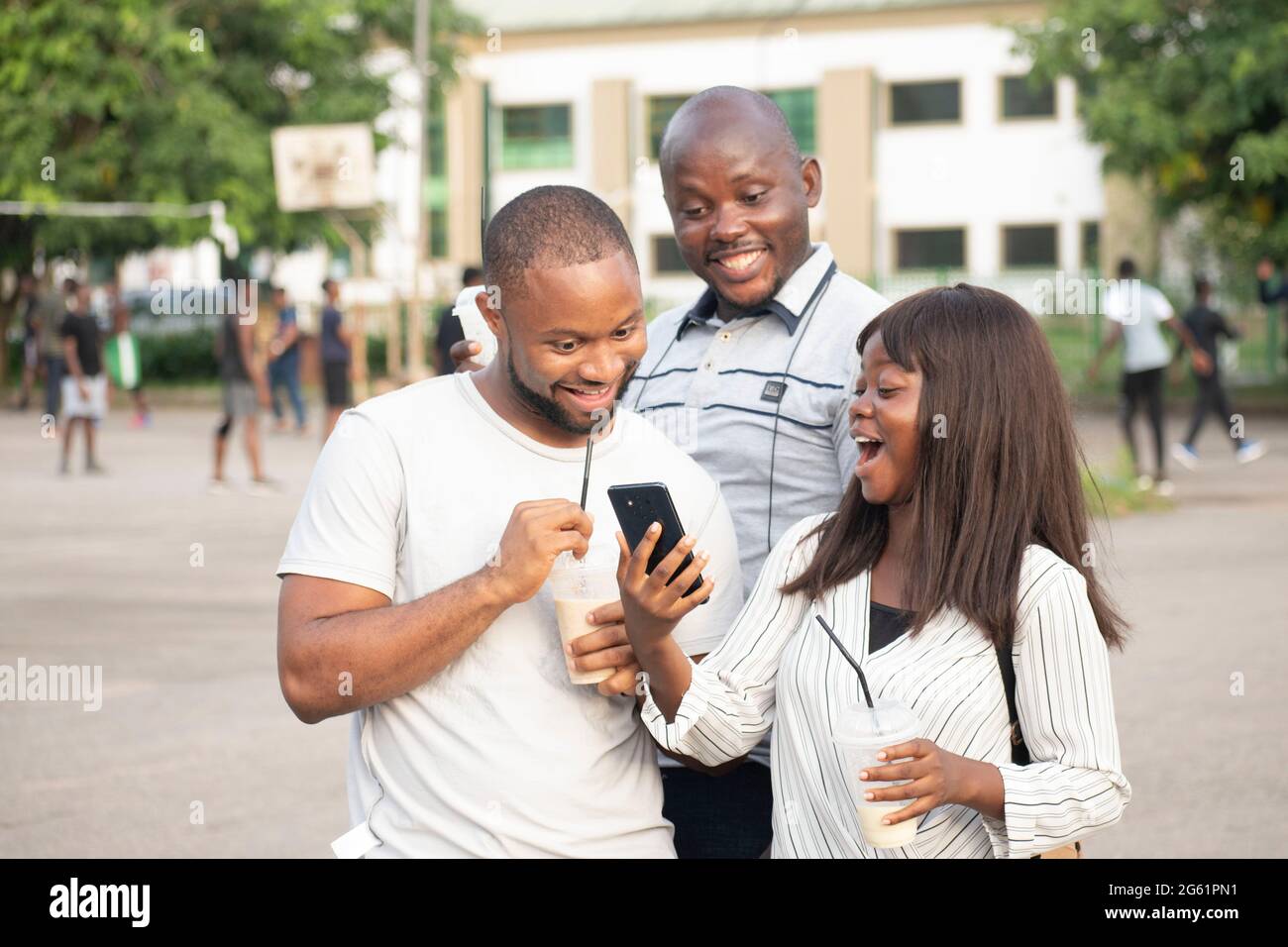 Drei junge afrikanische Menschen schauen im Freien in ihr Telefon Stockfoto