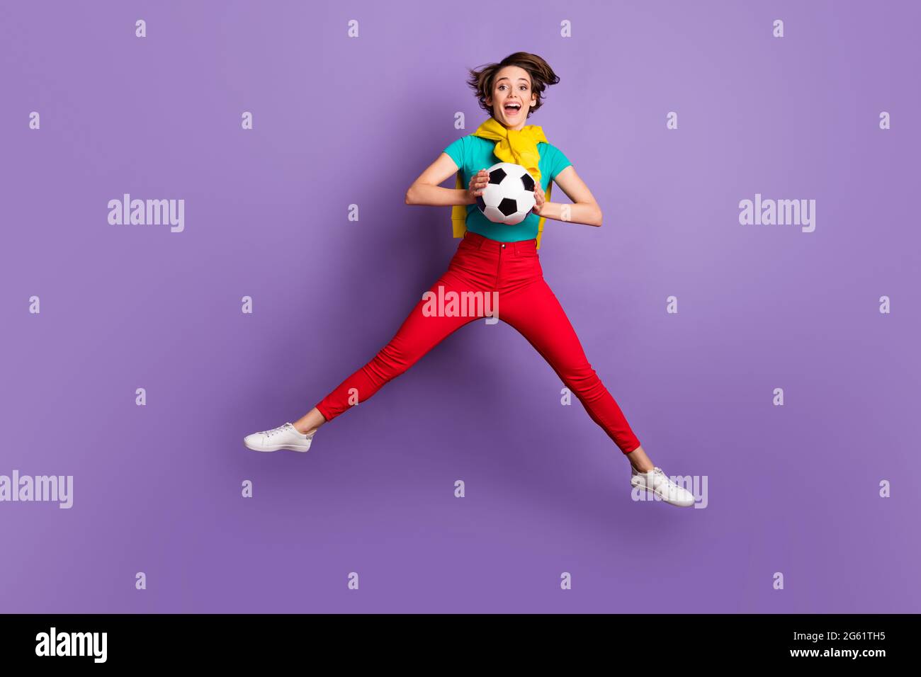 In voller Länge Foto von Dame springen halten Ball offen Mund tragen T-Shirt Hose Sneakers isoliert violette Farbe Hintergrund Stockfoto