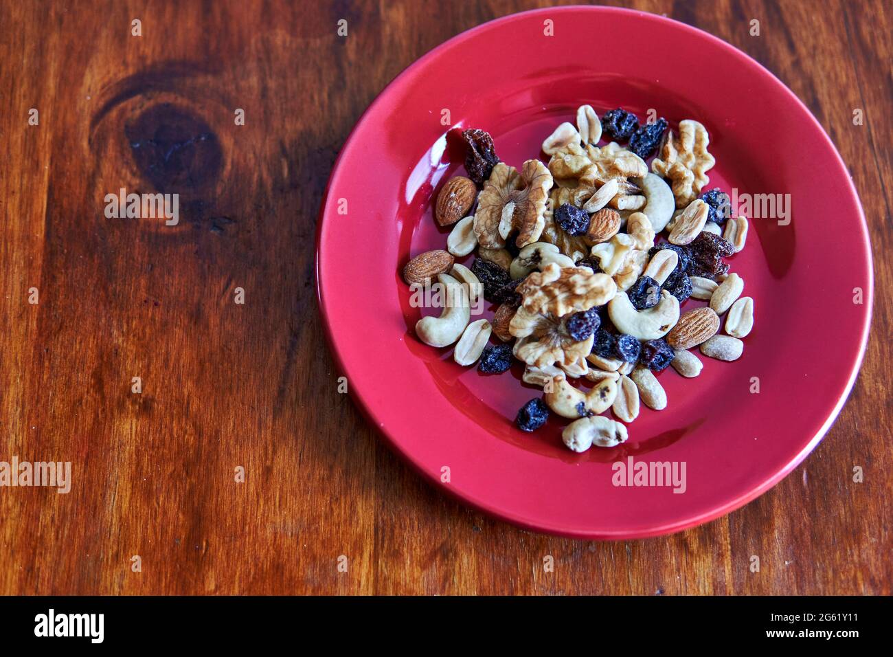 Rote Platte mit gemischten Nüssen getrockneten Früchten auf Holzgrund von oben. Gesunde Lebensmittel und Snacks. Walnuss, Pistazien, Mandeln, Haselnüsse und Cashewkerne. ho Stockfoto