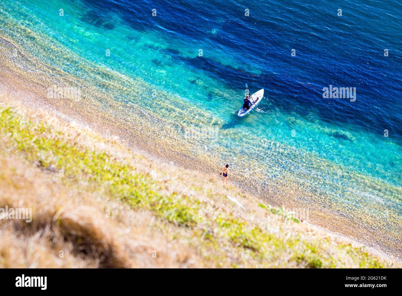 Frau, die ins Meer geht, und Mann auf einem Paddelbrett am man O'war Beach in Dorset, Jurassic Coast, Großbritannien Stockfoto