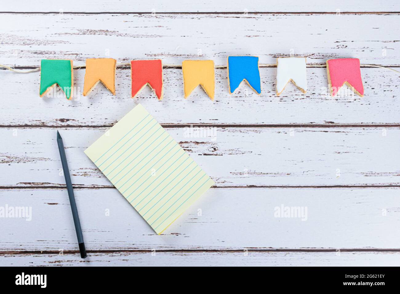 Notizblock neben einem Graphitstift und butterfarbenen Keksen in Form einer dekorativen brasilianischen Partyflagge. Stockfoto