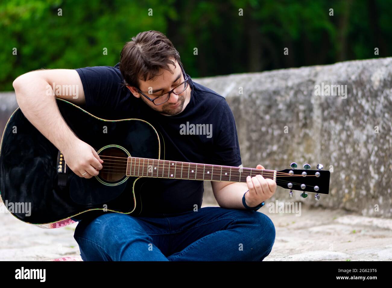 Junger Mann spielt Gitarre und sitzt auf der Brücke Stockfoto