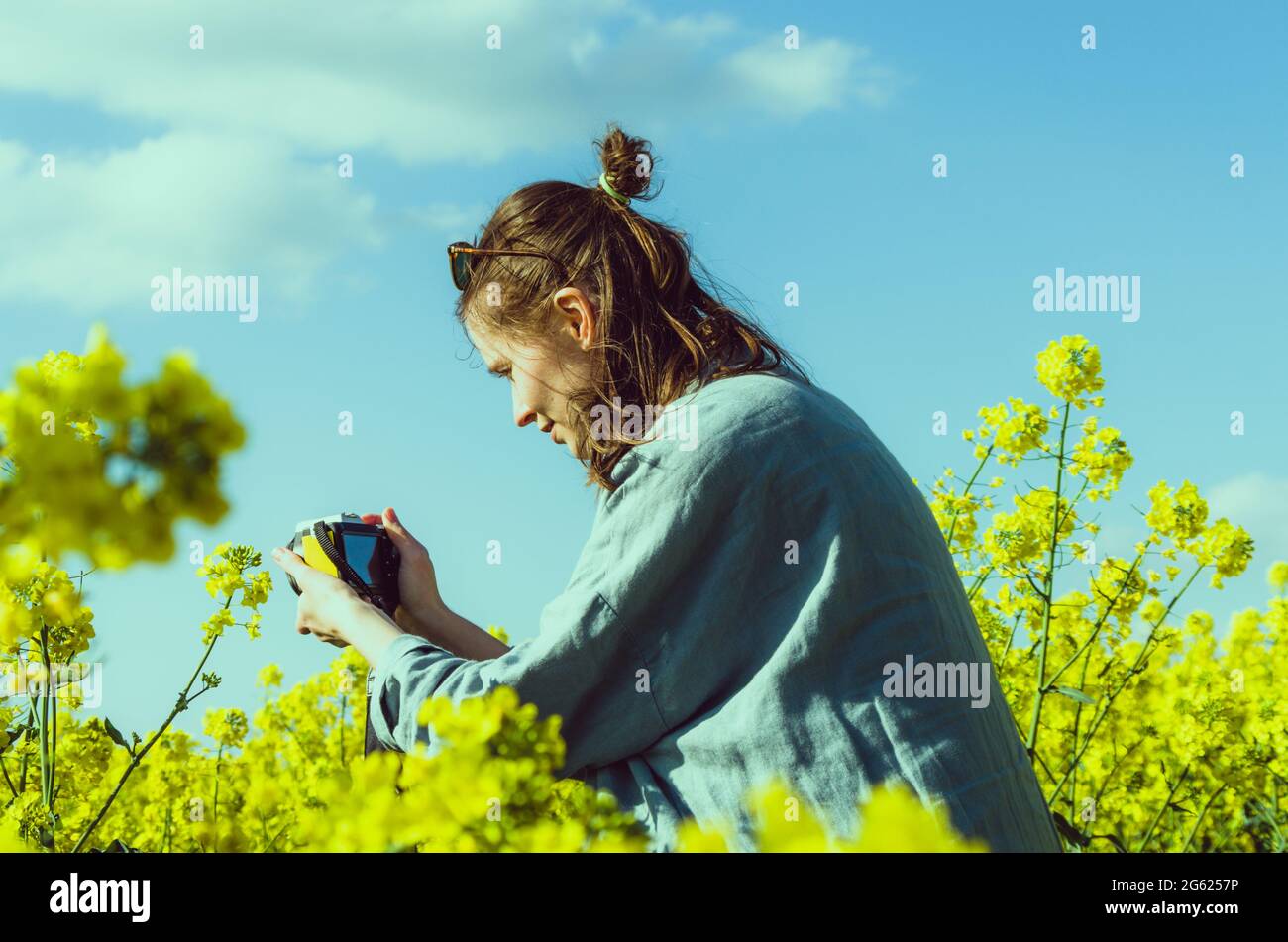 Fotografin auf einem Feld mit Rapsblumen mit gelber Kamera, die Details aus der Nähe fotografiert Stockfoto