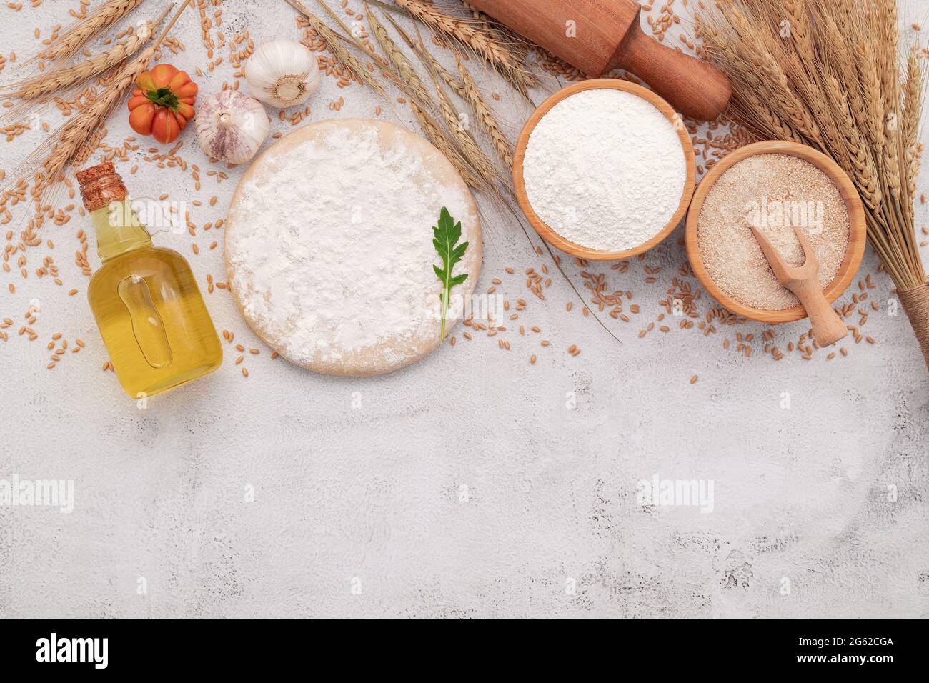 Die Zutaten für hausgemachten Pizzateig mit Weizenohren, Weizenmehl und Weizenkörnern auf weißem Beton-Hintergrund. Stockfoto