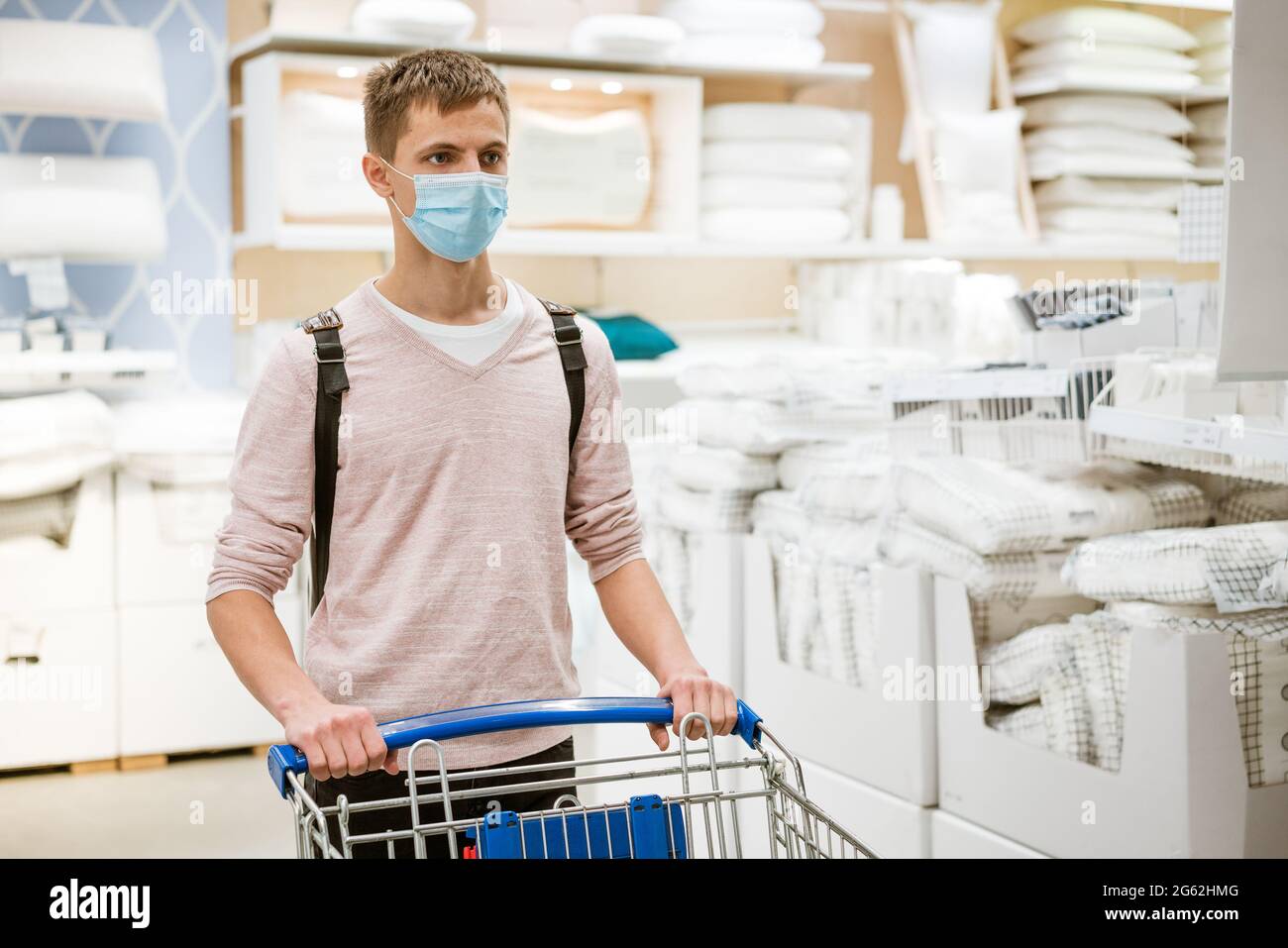 Ein Mann mit europäischem Auftritt in einer Schutzmaske und legerer Kleidung, mit einem Trolley im Geschäft in der Abteilung für alles für das Haus. Einkaufen während der Quarantäne Stockfoto