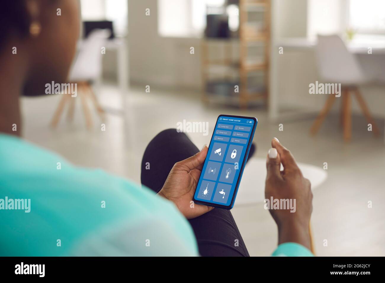 Die schwarze Frau steuert das System ihres Smart House über eine App auf ihrem Mobiltelefon Stockfoto