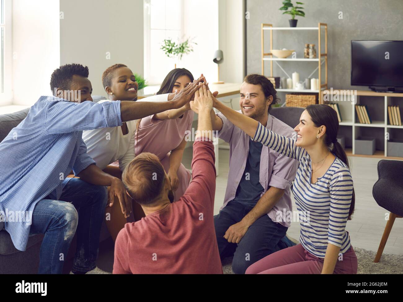Ein Team multinationaler Freunde hebt bei einem Treffen zu Hause die Hände und faltet sie zusammen. Stockfoto