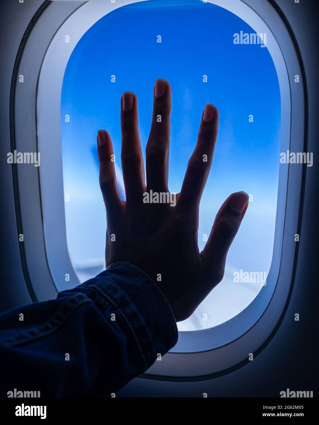 Eine Silhouette einer jungen erwachsenen männlichen Hand, die auf einem Flugzeugfenster platziert wird. Nostalgisches Reisekonzept. Stockfoto