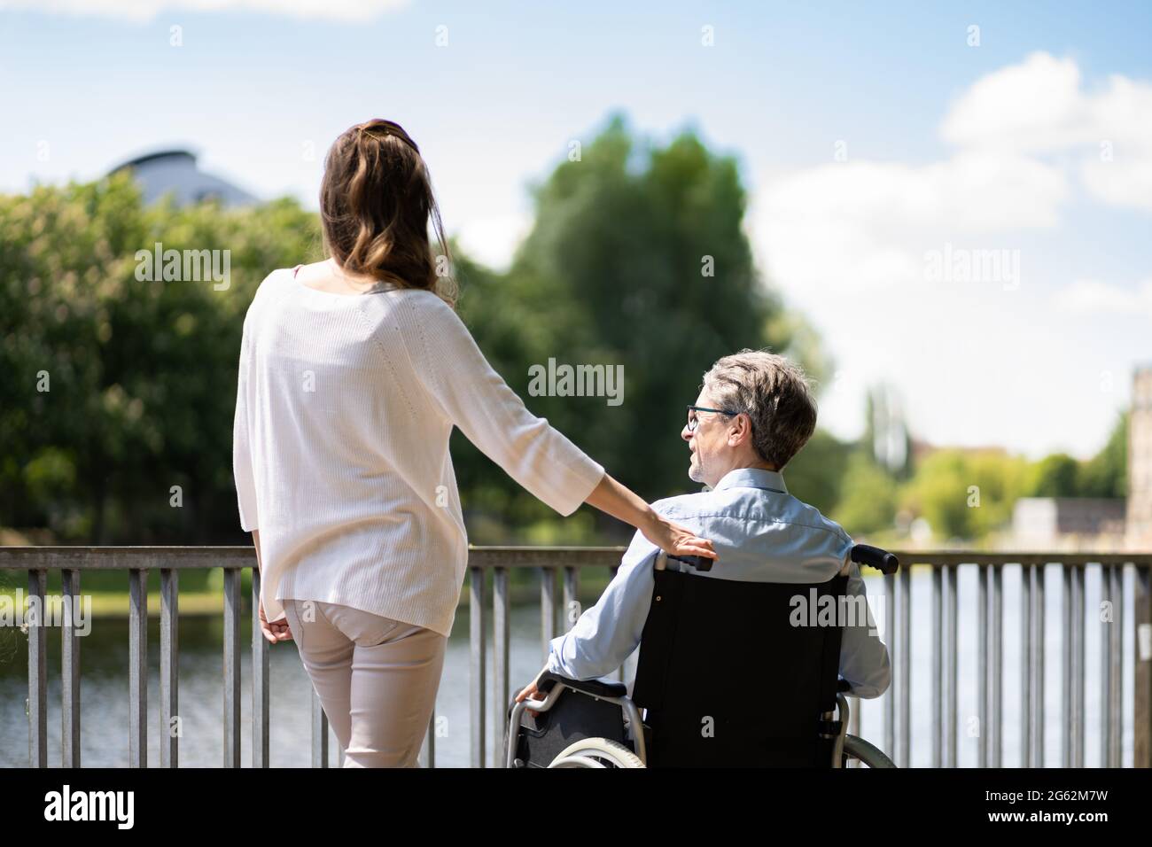 Seniorenbetreuung Und Rollstuhltransport. Lächelnde Frau Schiebt Älteren Mann Stockfoto