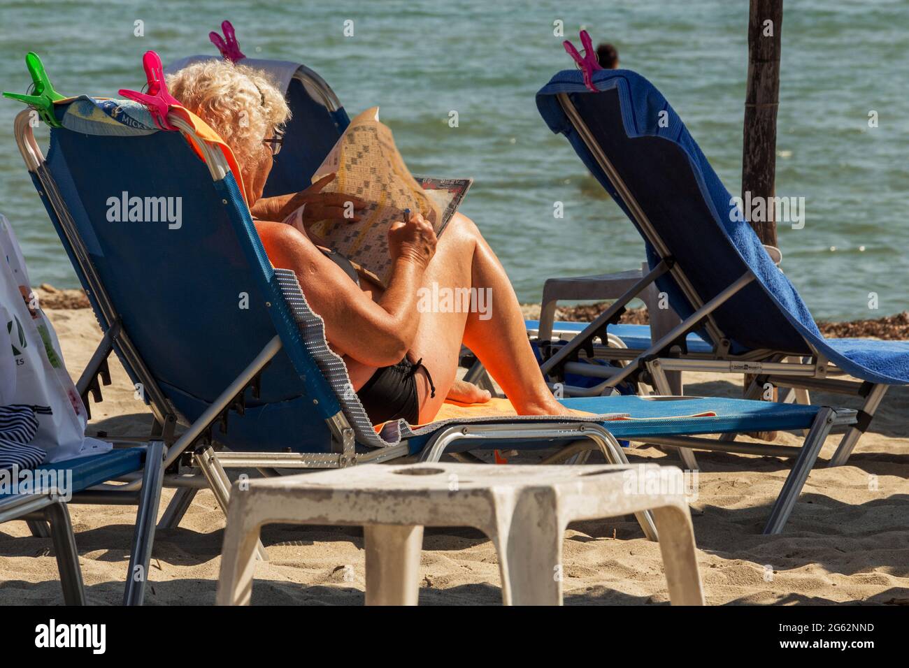 Rückansicht einer Frau, die am Strand ein Kreuzworträtsel löst Stockfoto