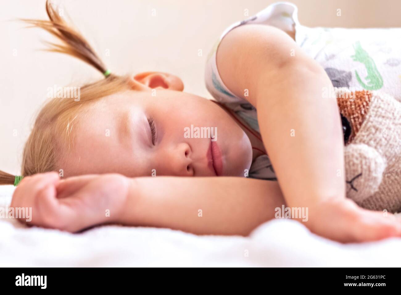 Ein kleines Mädchen Kleinkind schläft auf einem Bett mit Spielzeug gekuschelt. Kindheit Stockfoto