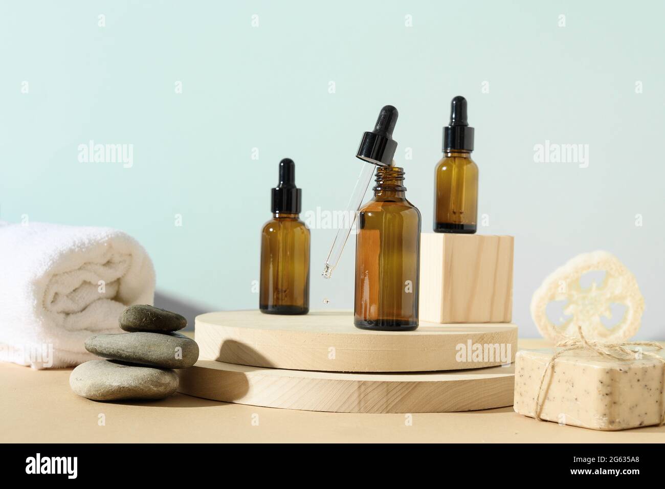 Minimale moderne natürliche Zusammensetzung mit Kosmetiköl in Flaschen, Naturstein, Loofa auf Ständer auf beige und blauem Hintergrund. SPA-Set für die Körperpflege. Stockfoto