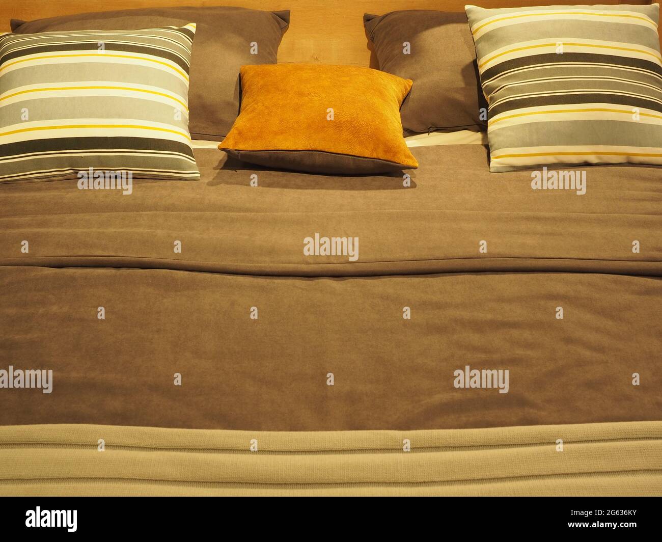 Bettfragment mit gestreiften und monochromen quadratischen Kissen und einer Decke in graubraunen Farbtönen Stockfoto