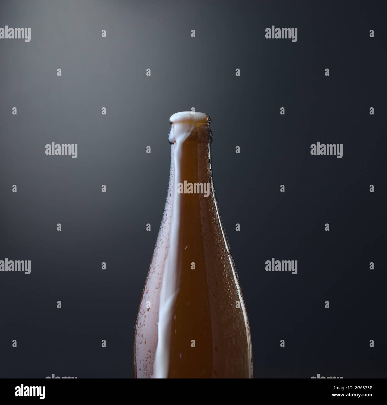 Vorderansicht einer Flasche kaltes Bier mit überlauftem Schaum vor dunkelblauem Grunge-Hintergrund. Kaltes alkoholisches Getränk, internationales Biertagskonzept. Stockfoto