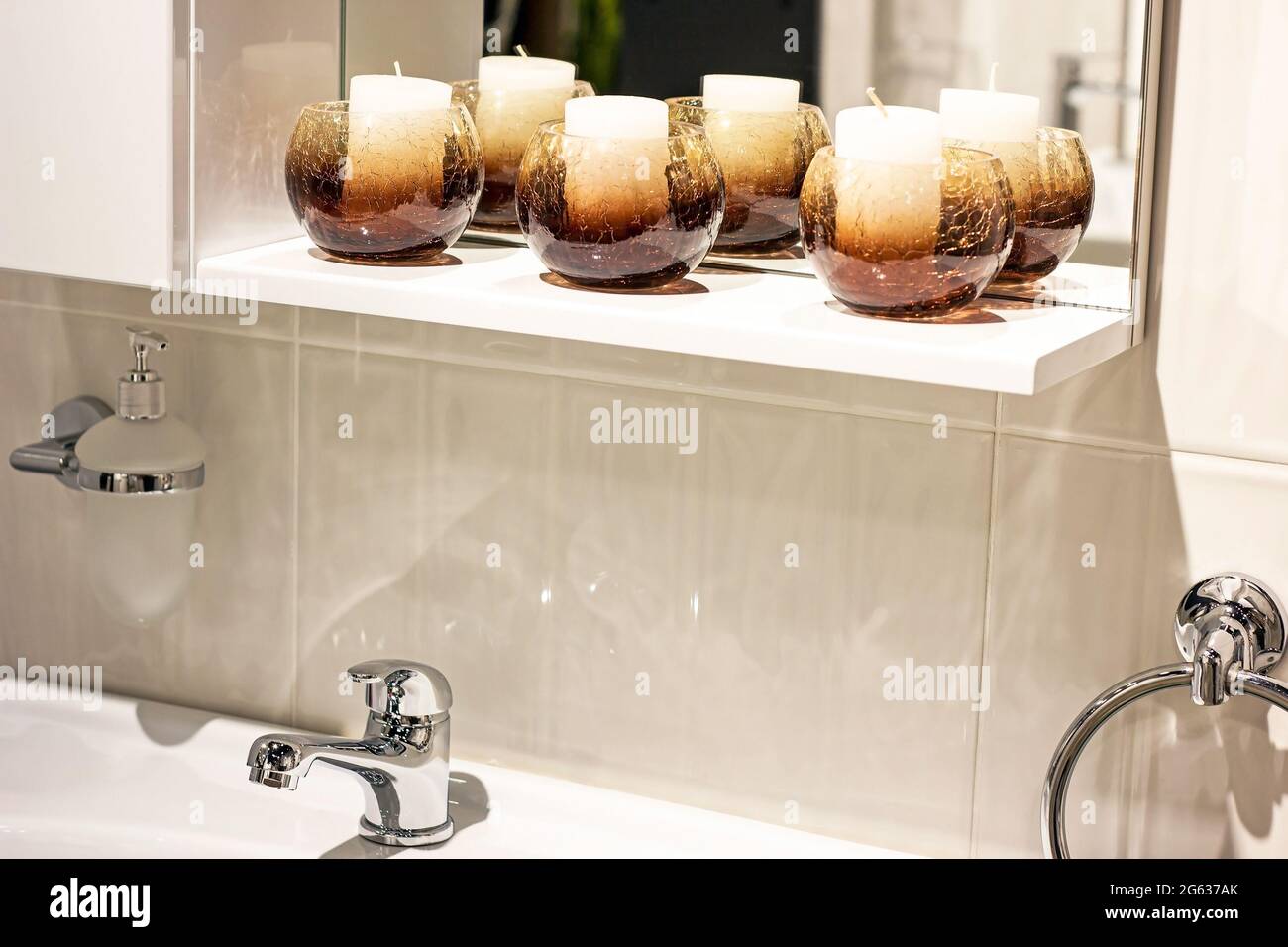 Neuer moderner Metallwasserhahn mit dem weißen Waschbecken und Kerzen auf dem Keramikfliesen-Wandhintergrund im Badezimmer. Stockfoto