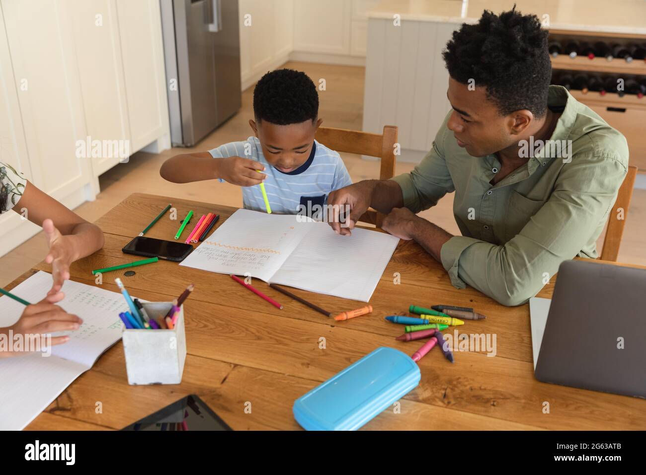 Glücklicher afroamerikanischer Vater mit Tochter und Sohn, die zu Hause Hausaufgaben machen, lächelnd Stockfoto