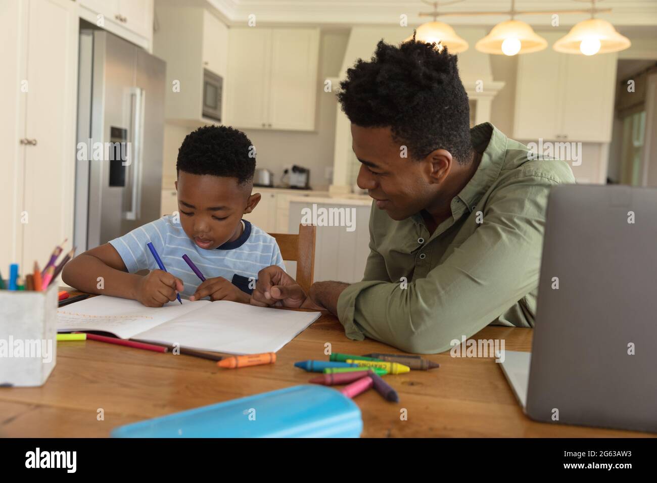 Glücklicher afroamerikanischer Vater mit Sohn, der zu Hause Hausaufgaben macht und lächelt Stockfoto