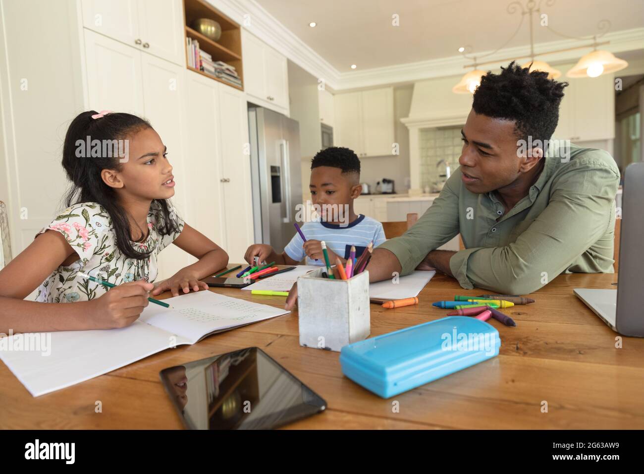 Glücklicher afroamerikanischer Vater mit Tochter und Sohn, die zu Hause Hausaufgaben machen, lächelnd Stockfoto