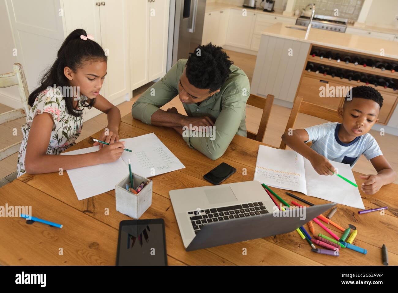 Glücklicher afroamerikanischer Vater mit Tochter und Sohn, die zu Hause Hausaufgaben machen, lächelnd Stockfoto