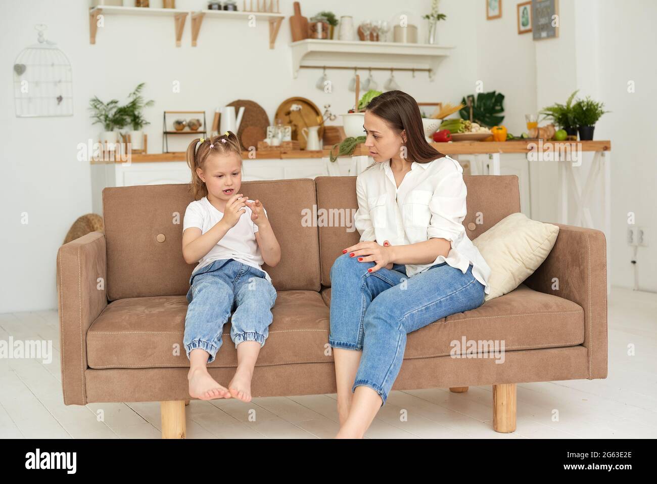 Das vertrauensvolle Verhältnis von Mutter und Tochter. Gespräch einer Frau mit einem kleinen Mädchen zu Hause auf der Couch in der Küche. Beste Freunde glücklich Motte Stockfoto