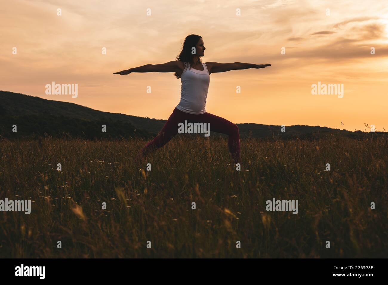 Silhouette einer Frau, die Yoga/Virabhadrasana praktiziert, Kriegerpose. Stockfoto