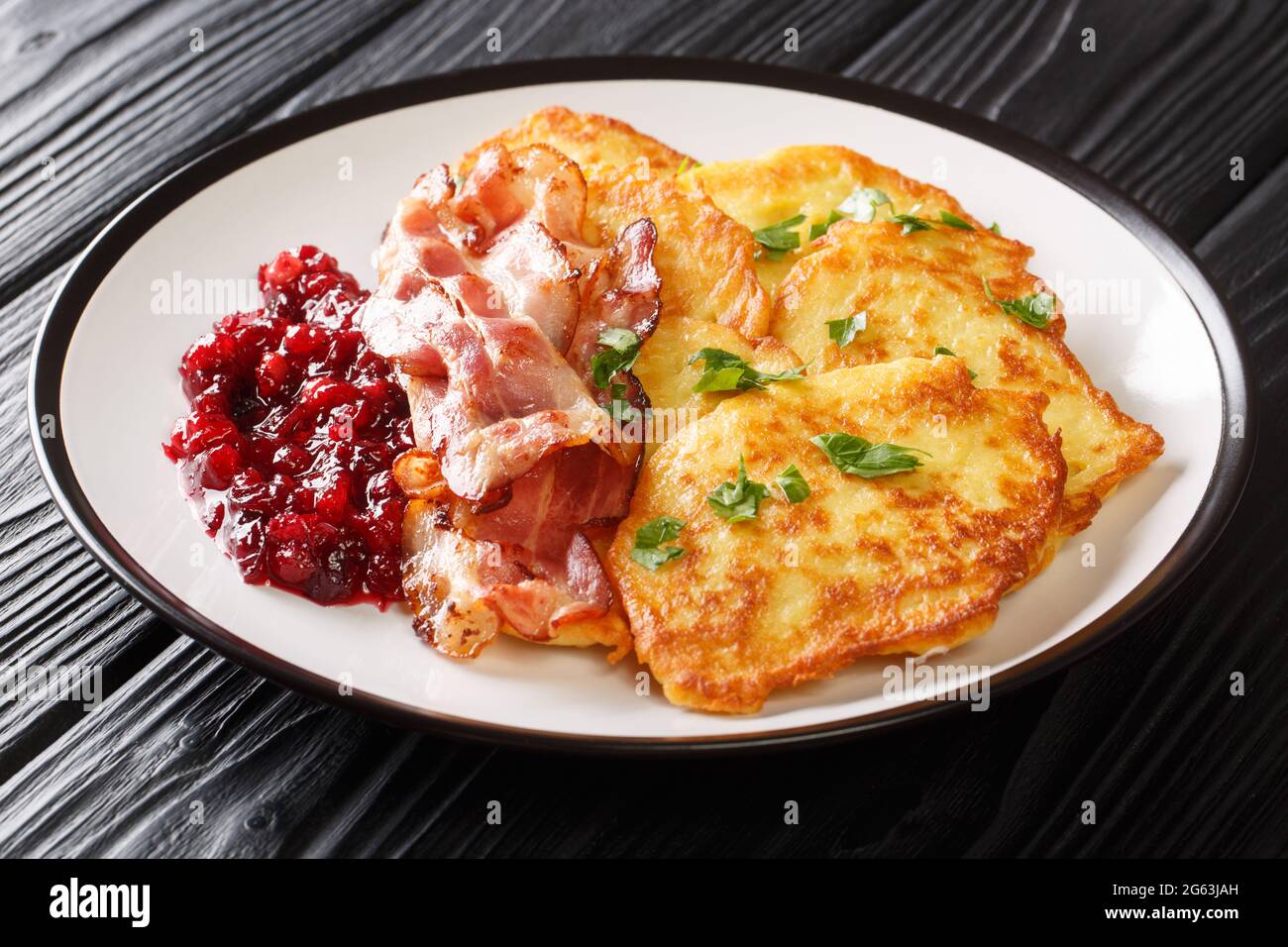 Knusprig gebratene Kartoffelpfannkuchen mit Preiselbeermarmelade und Speck aus der Nähe auf einem Teller auf dem Tisch. Horizontal Stockfoto