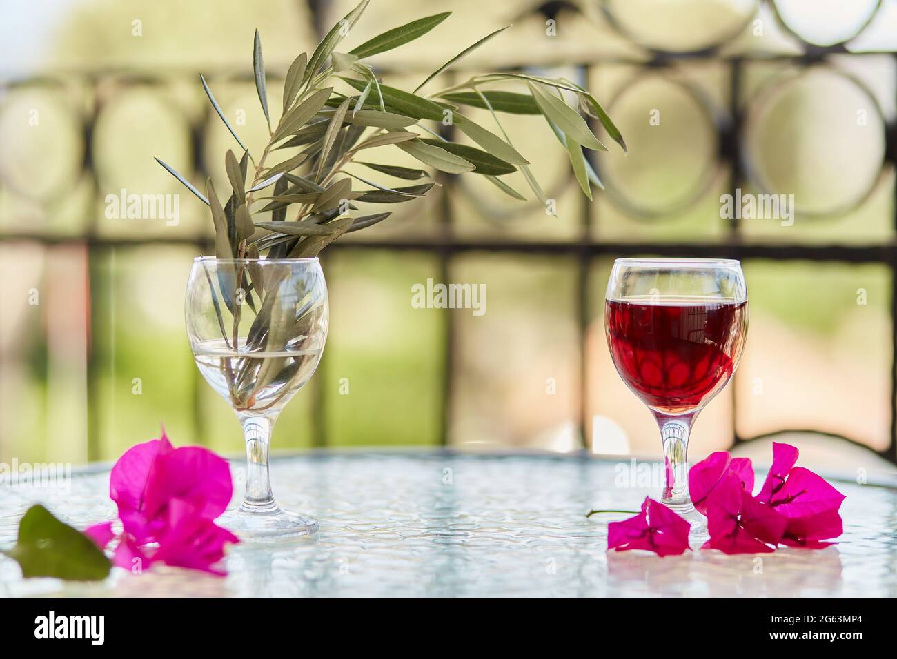 Elegantes und farbenfrohes Glas Rotwein. Dekorative rosa Blüten von Bougainvillea in einem Glas. Festliches Weihnachtskonzept. Sommerhintergrund. Dekorativ gr Stockfoto
