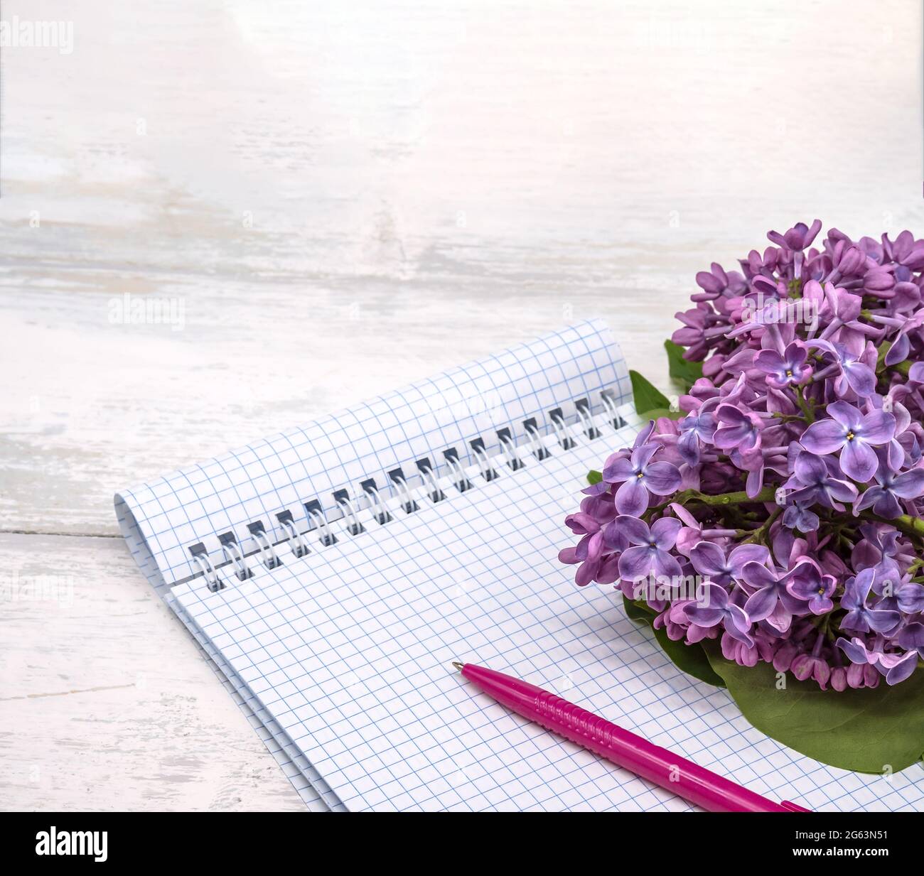 Ein Notizbuch und eine Blume. Ein Notizbuch mit einem Stift und Blumen. Spiralnotizbuch und Stift. Copybook auf einem hölzernen Hintergrund. Stockfoto