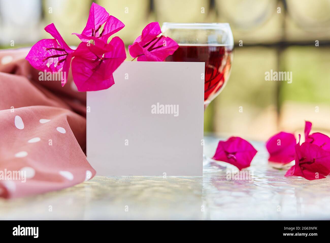 Trendiges Glas Rotwein. Dekorative rosa Blüten von Bougainvillea. Elegante Nachbau von Postkarte oder Einladung. Festliches Weihnachtskonzept. Dekorativer gre Stockfoto