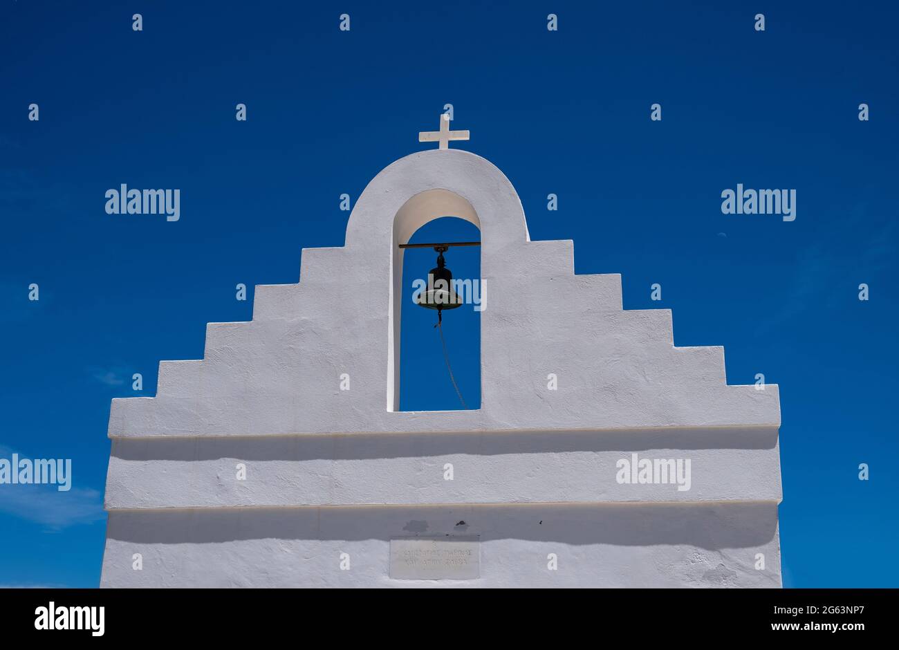 Griechische Insel, Kykladen Griechenland. Traditionelle weißgetünchte orthodoxe Kirche mit religiösem Kreuz und Glocke vor klarem blauen Himmel Hintergrund. Sommerromanti Stockfoto