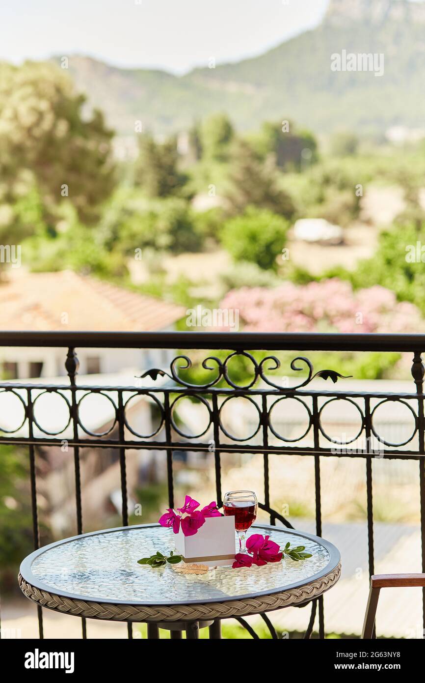 Ein Glas Rotwein auf dem Tisch auf der Terrasse. Dekorative rosa Blüten von Bougainvillea und goldenen Federzeichen. Nachbau einer Postkarte oder Einladung. Ro Stockfoto