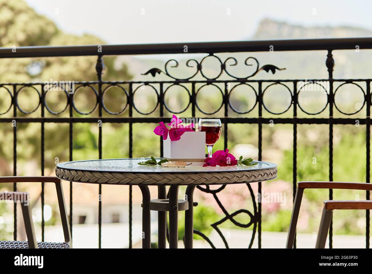 Ein Glas Rotwein auf dem Tisch auf der Terrasse. Dekorative rosa Blüten von Bougainvillea. Nachbau einer Postkarte oder Einladung. Romantisches Dinner-Konzept. Stockfoto