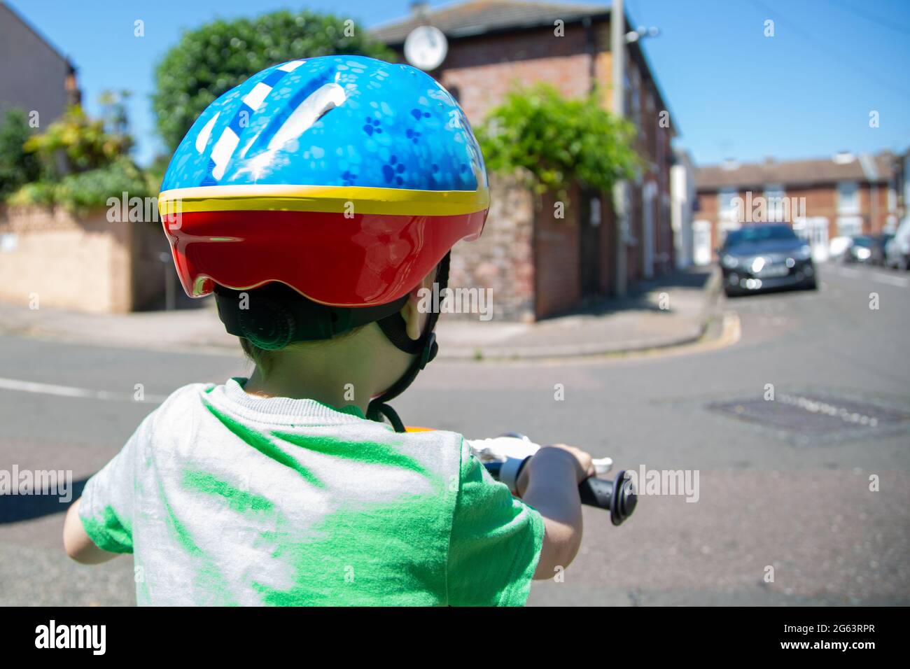 Ein kleines Kind, das mit einem Fahrradhelm auf einem Fahrrad unterwegs ist, um die Straße zu überqueren Stockfoto