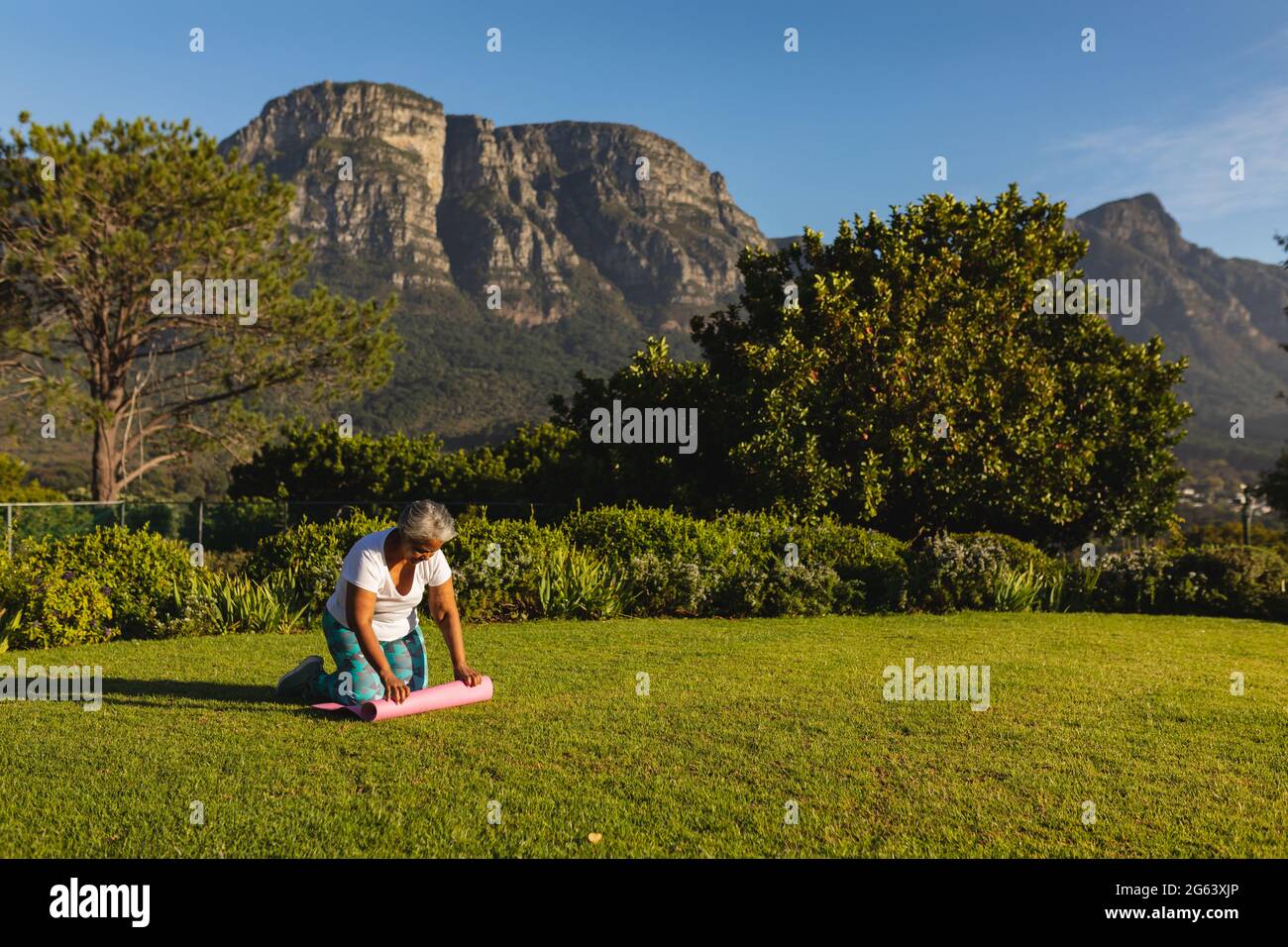 Eine ältere afroamerikanische Frau, die in einer atemberaubenden Landschaft eine Yogamatte auf Gras legt Stockfoto