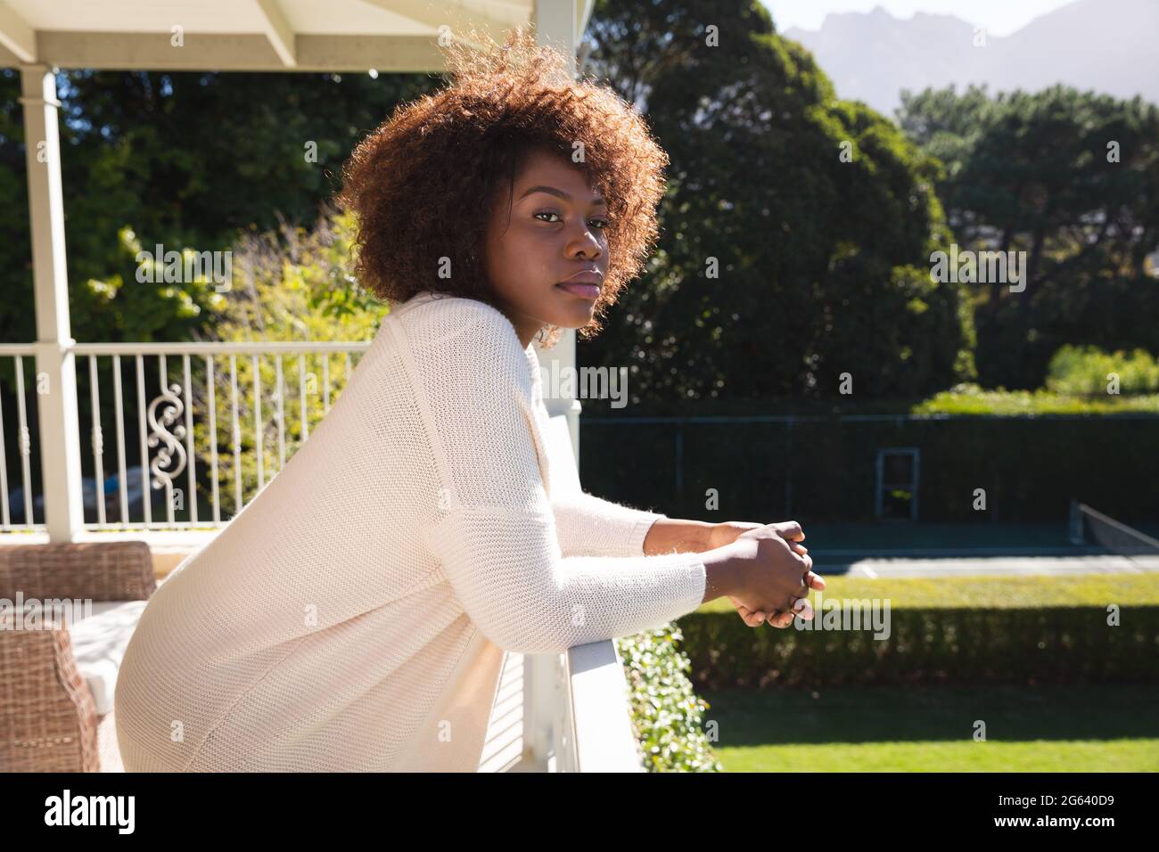 Glückliche afroamerikanische Frau, die sich auf dem sonnigen Balkon des Landhauses entspannt und die Aussicht genießt Stockfoto