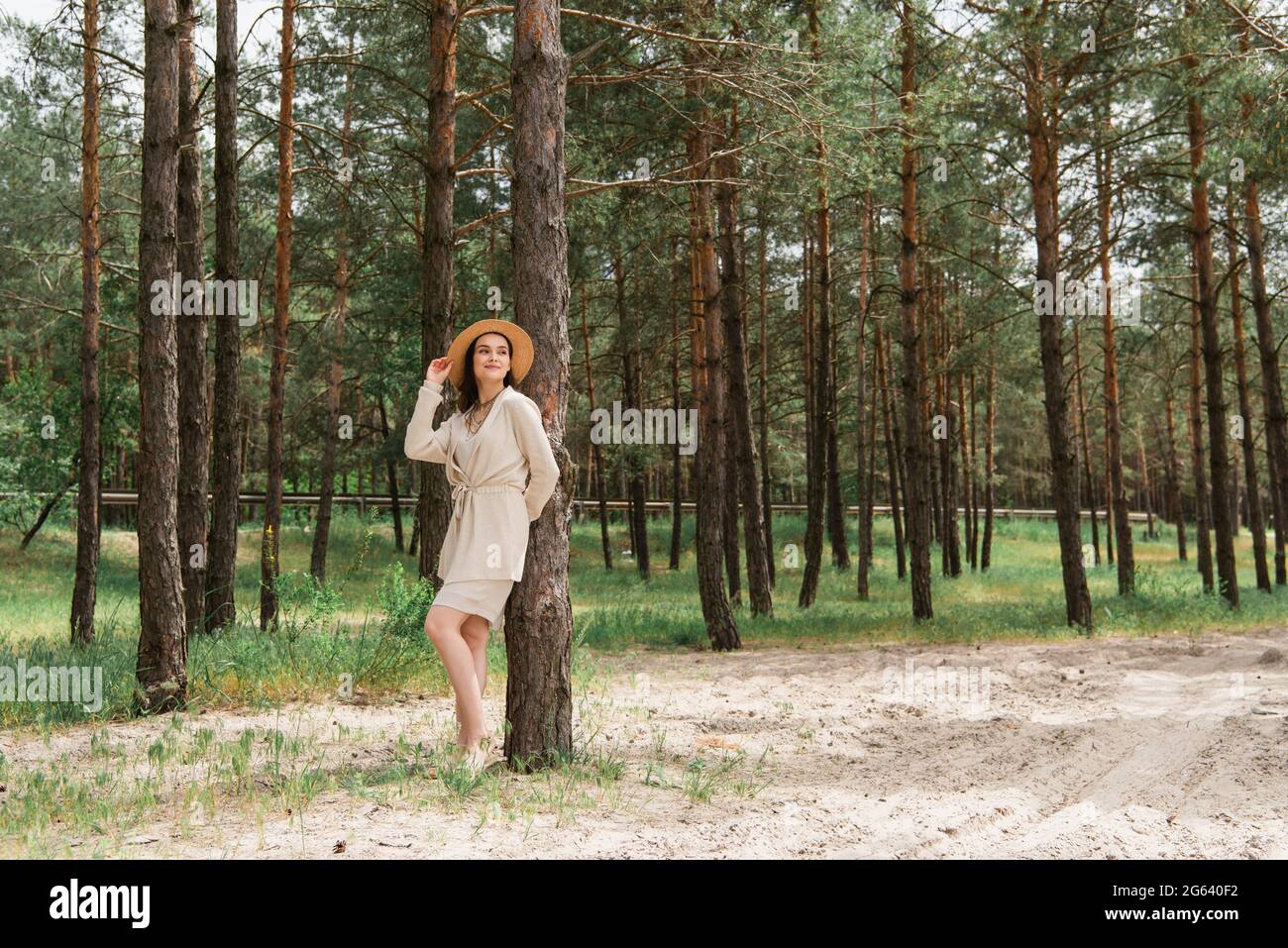 Volle Länge der fröhlichen jungen Frau Anpassung Strohhut und im Wald stehen Stockfoto