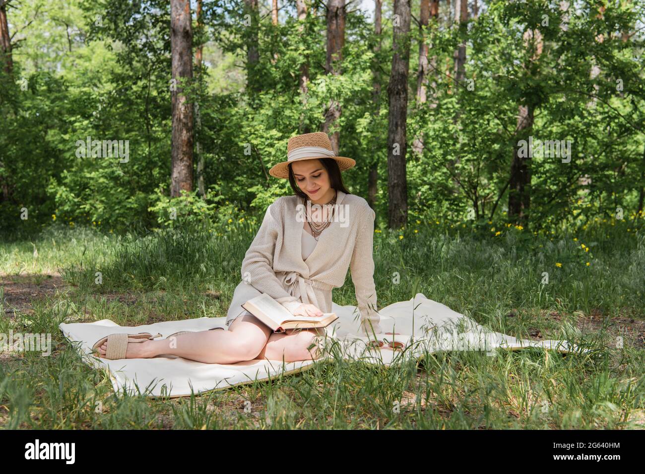 Glückliche junge Frau im Strohhut Buch im Wald lesen Stockfoto