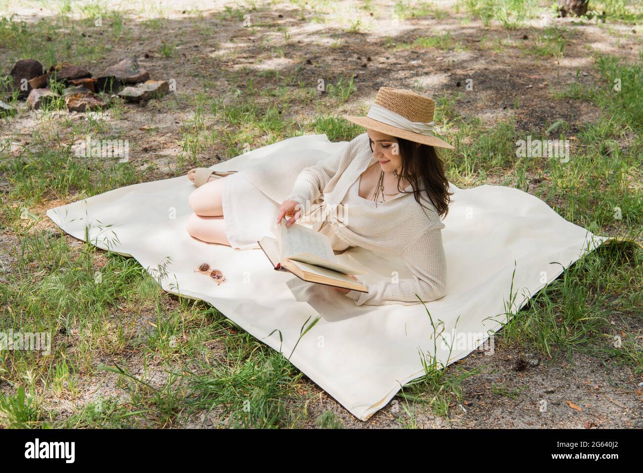 Positive junge Frau im Strohhut Buch im Wald lesen Stockfoto