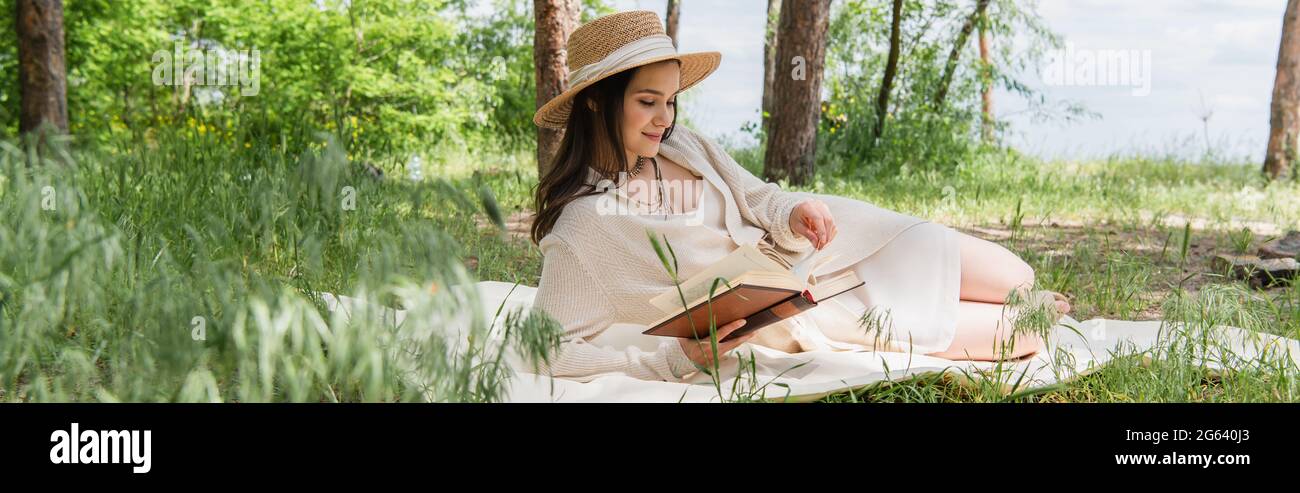 Fröhliche junge Frau im Strohhut, die Buch im Wald liest, Banner Stockfoto
