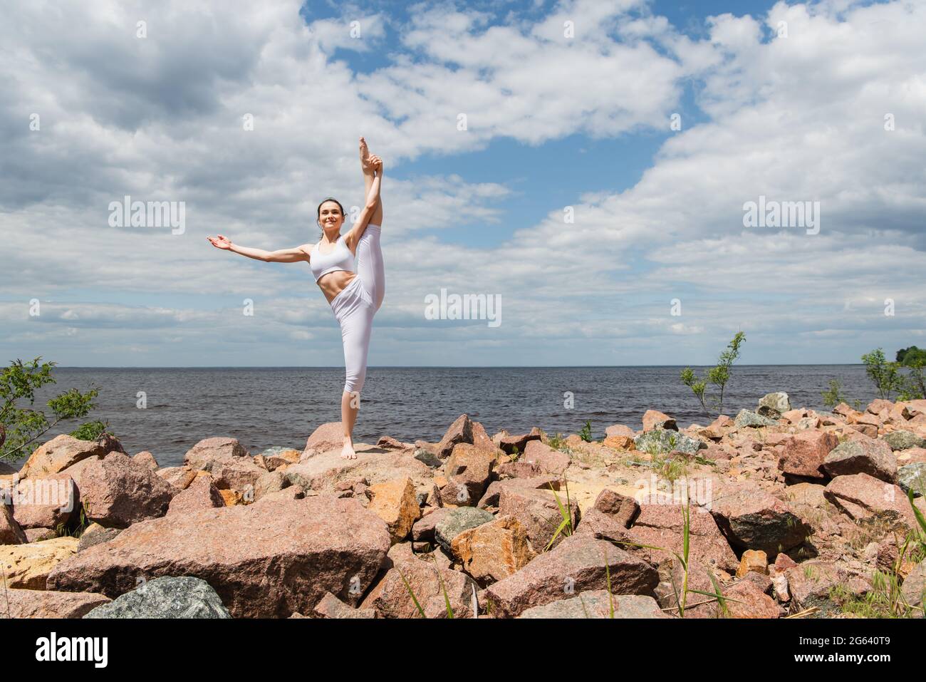 Glückliche Frau in Sportswear, die Hand bis Fuß in der Nähe des Meeres steht Stockfoto