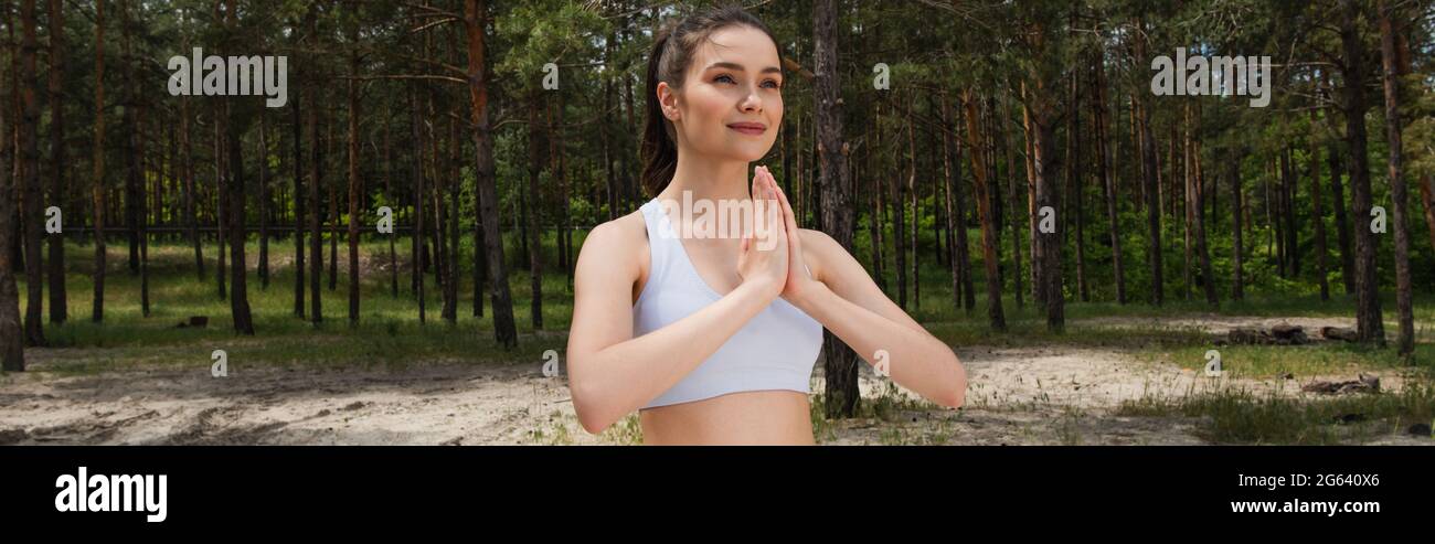 Lächelnde junge Frau mit betenden Händen im Wald, Banner Stockfoto