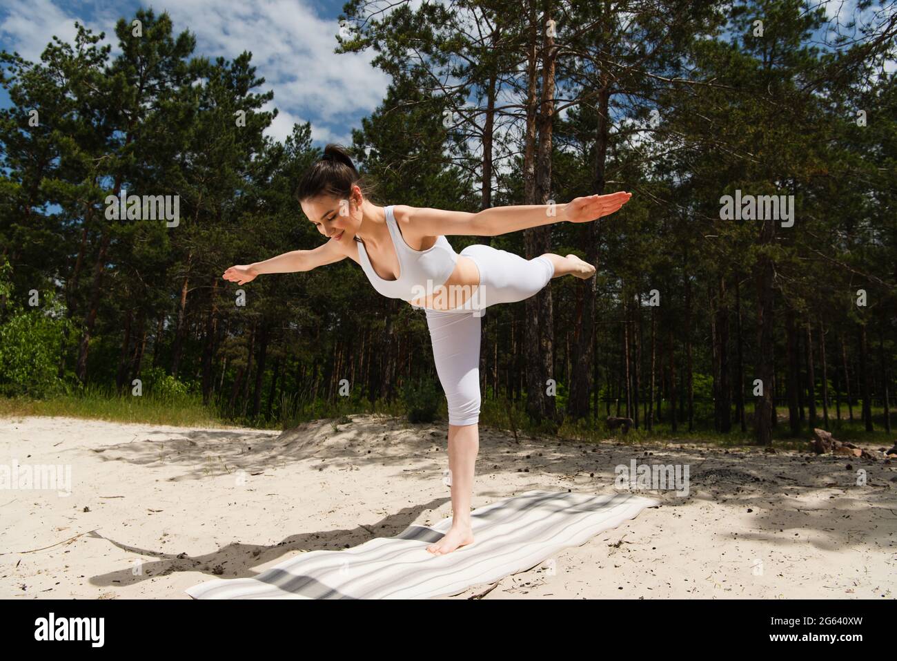 Barfuß Frau in Sportkleidung stehend in Kriegeryogahaltung mit ausgestreckten Händen draußen Stockfoto