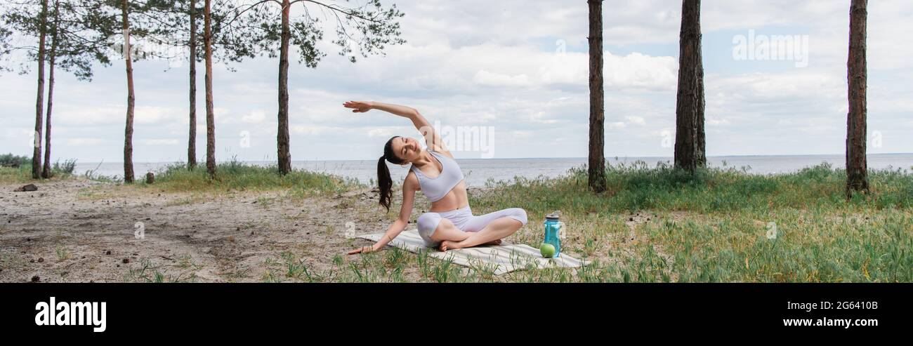 Junge Frau, die mit gekreuzten Beinen sitzt und sich im Wald ausdehnt, Banner Stockfoto