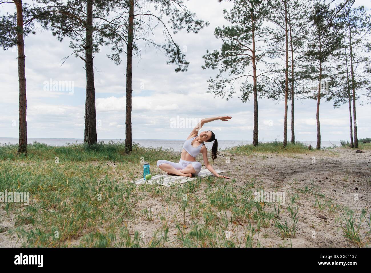 Brünette junge Frau in Sportkleidung sitzt in Lotuspose und Strecken auf Yoga-Matte Stockfoto